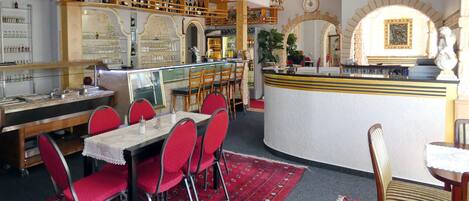A restaurant with a bar area, red upholstered chairs, and a patterned carpet.