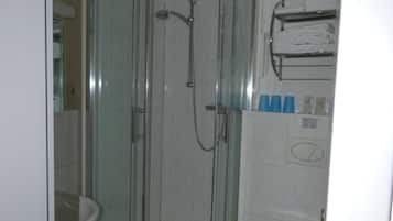 A glass-enclosed shower stall with a handheld showerhead, a toilet, and a towel rack with folded towels.