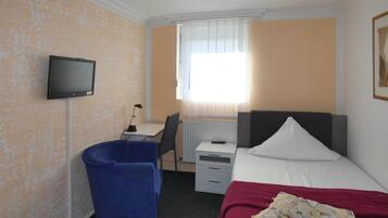 A hotel room with a bed, a desk, a chair, a television, and a radiator.