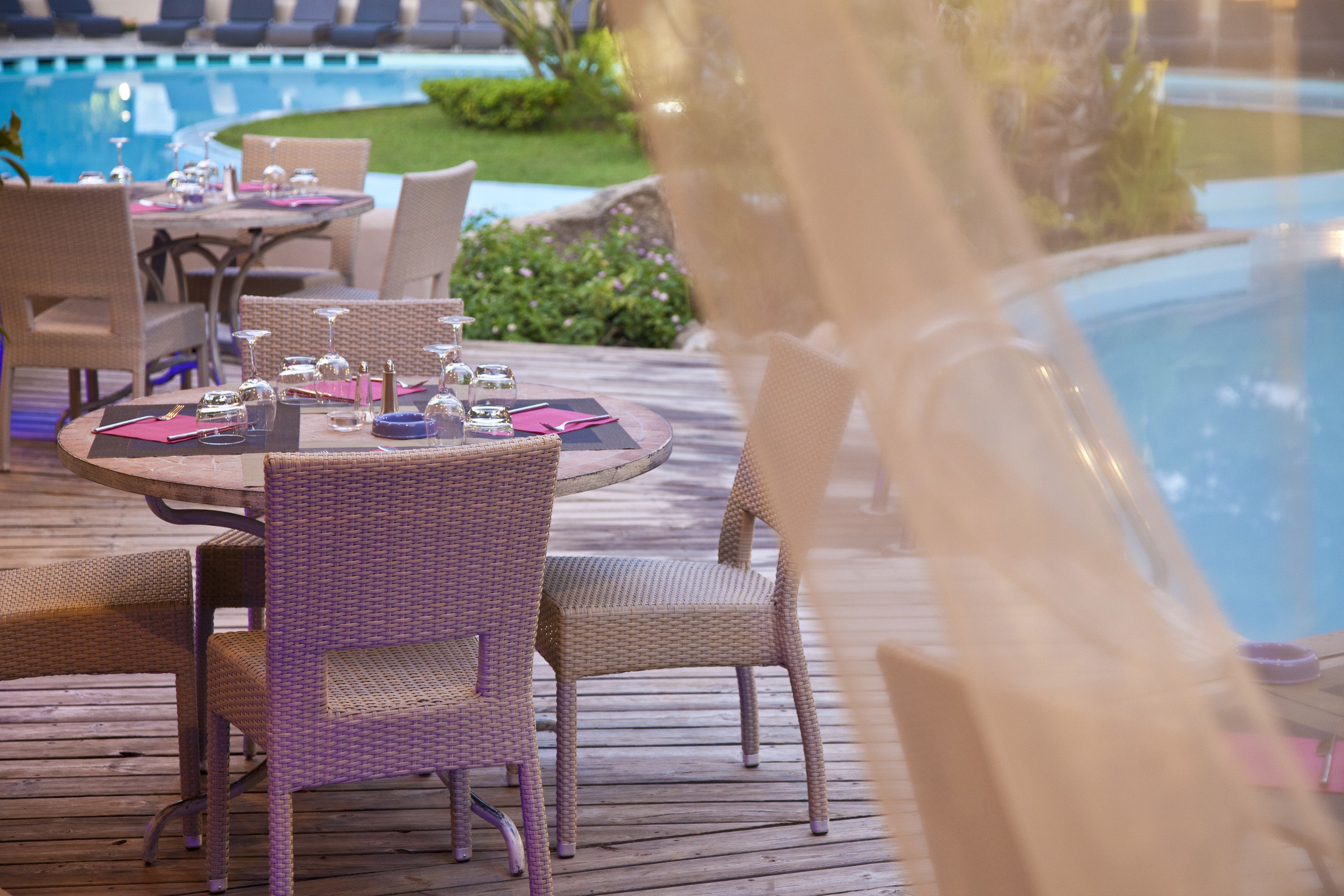A poolside dining area with wicker furniture and a table set for two.