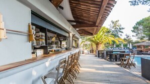 Zona de bar al aire libre con techado, sillas de madera y ambiente junto a la piscina.