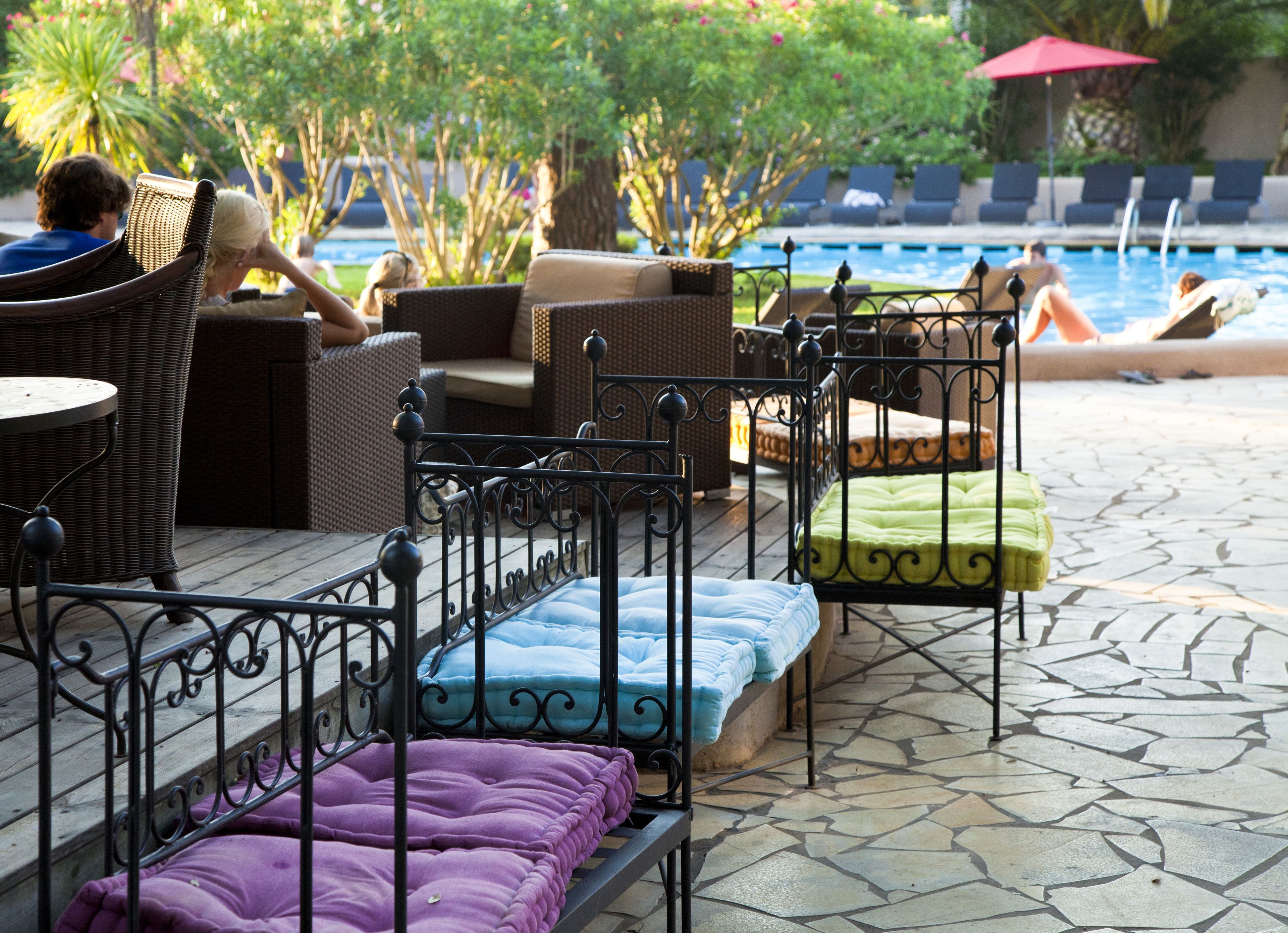 Un área junto a la piscina con muebles de mimbre y camas metálicas con cojines de colores.