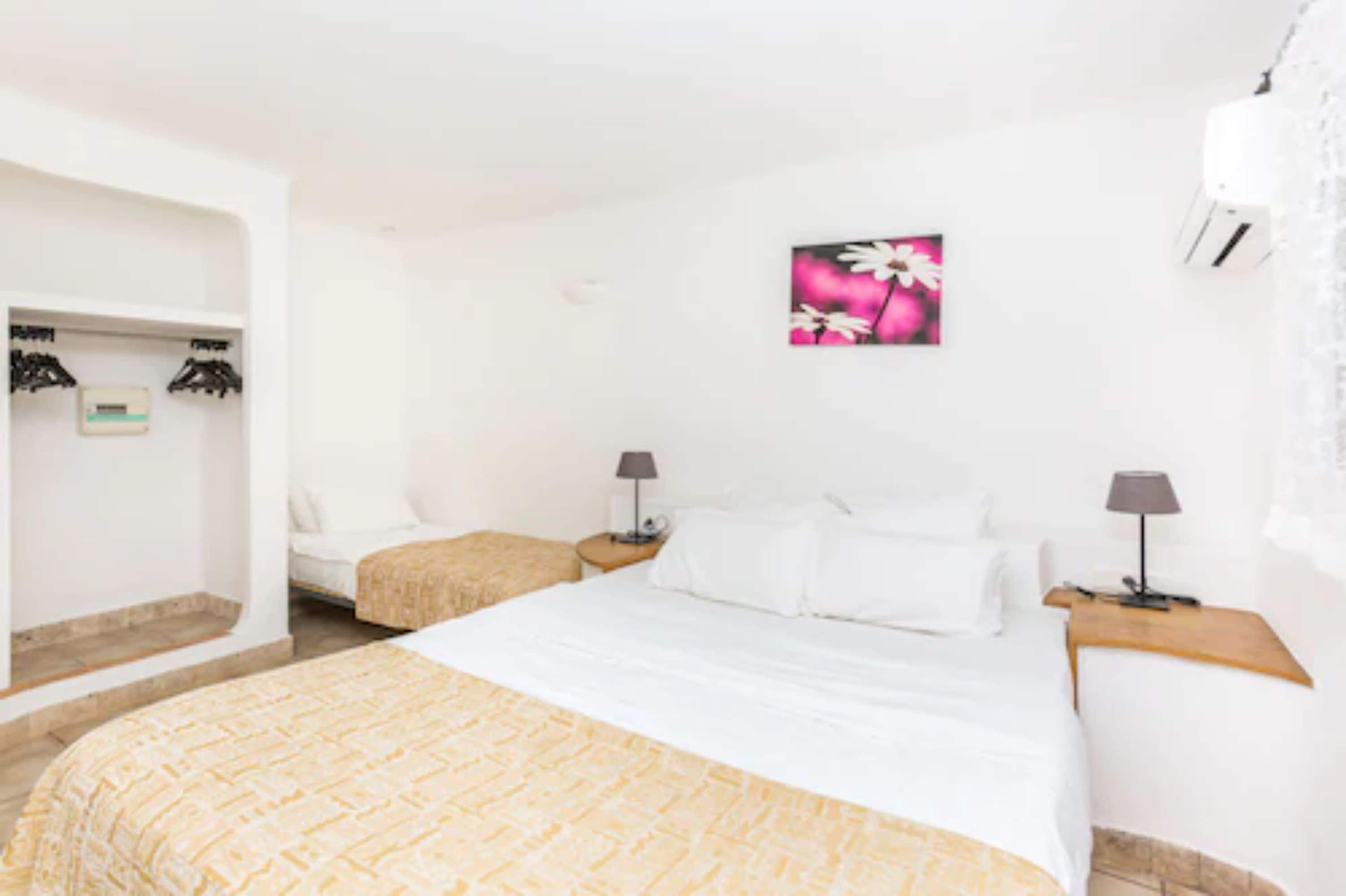 A hotel room with a large bed, two bedside tables with lamps, a wardrobe, and a painting on the wall.