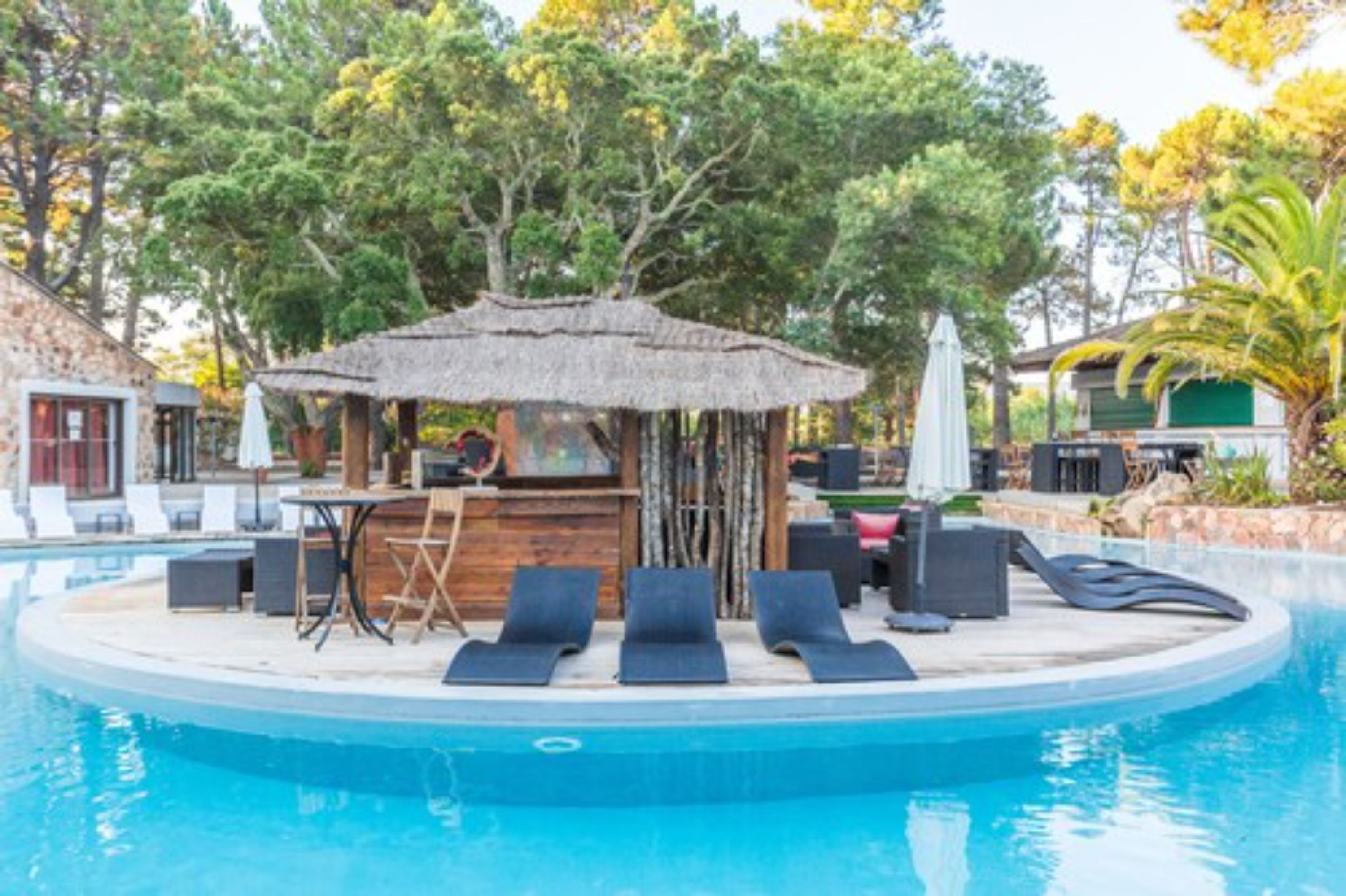 Un área junto a la piscina con sillas de descanso, un bar y una estructura de techo de paja.