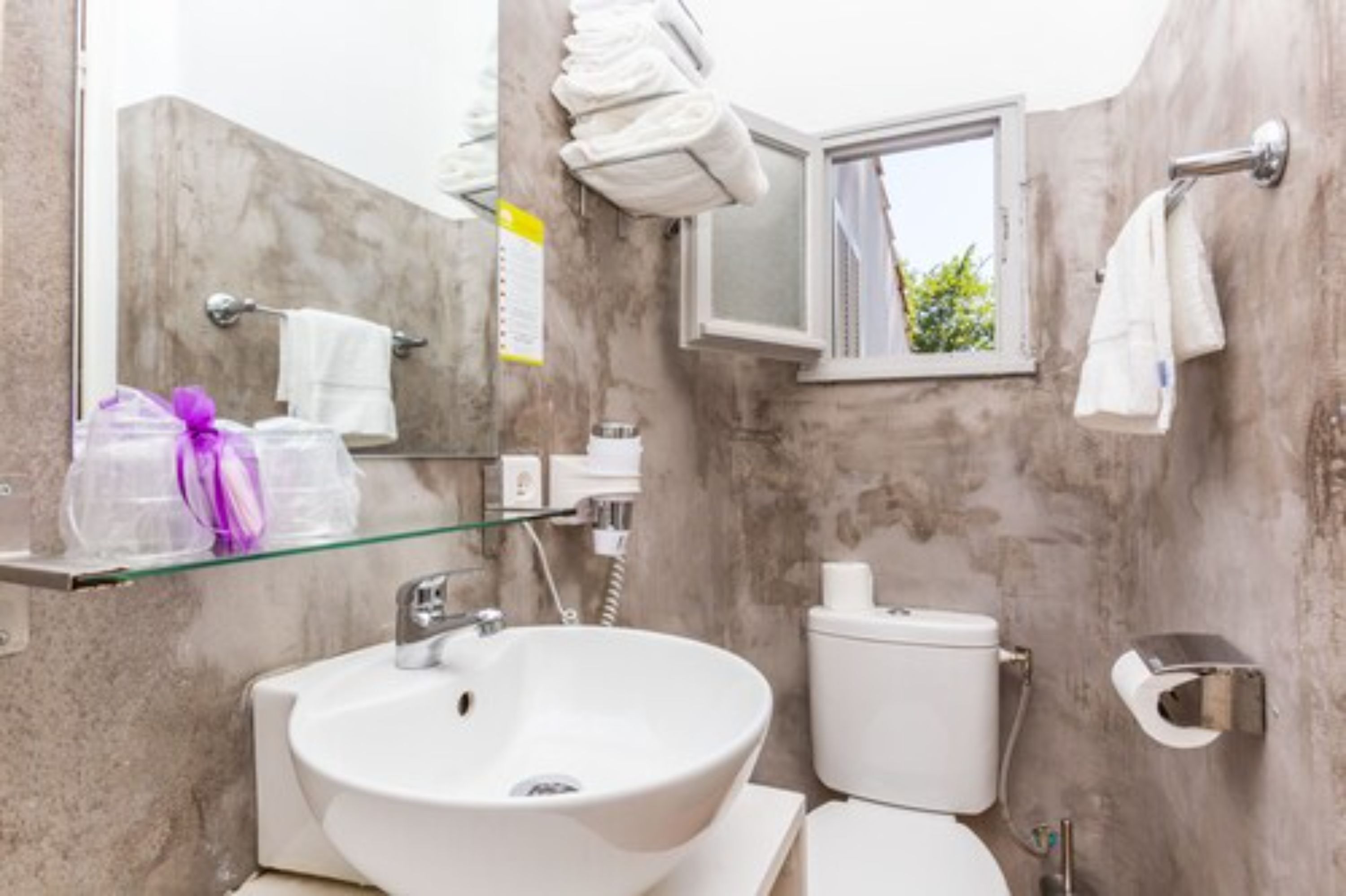 A bathroom with a white sink, toilet, and a glass shelf with toiletries.