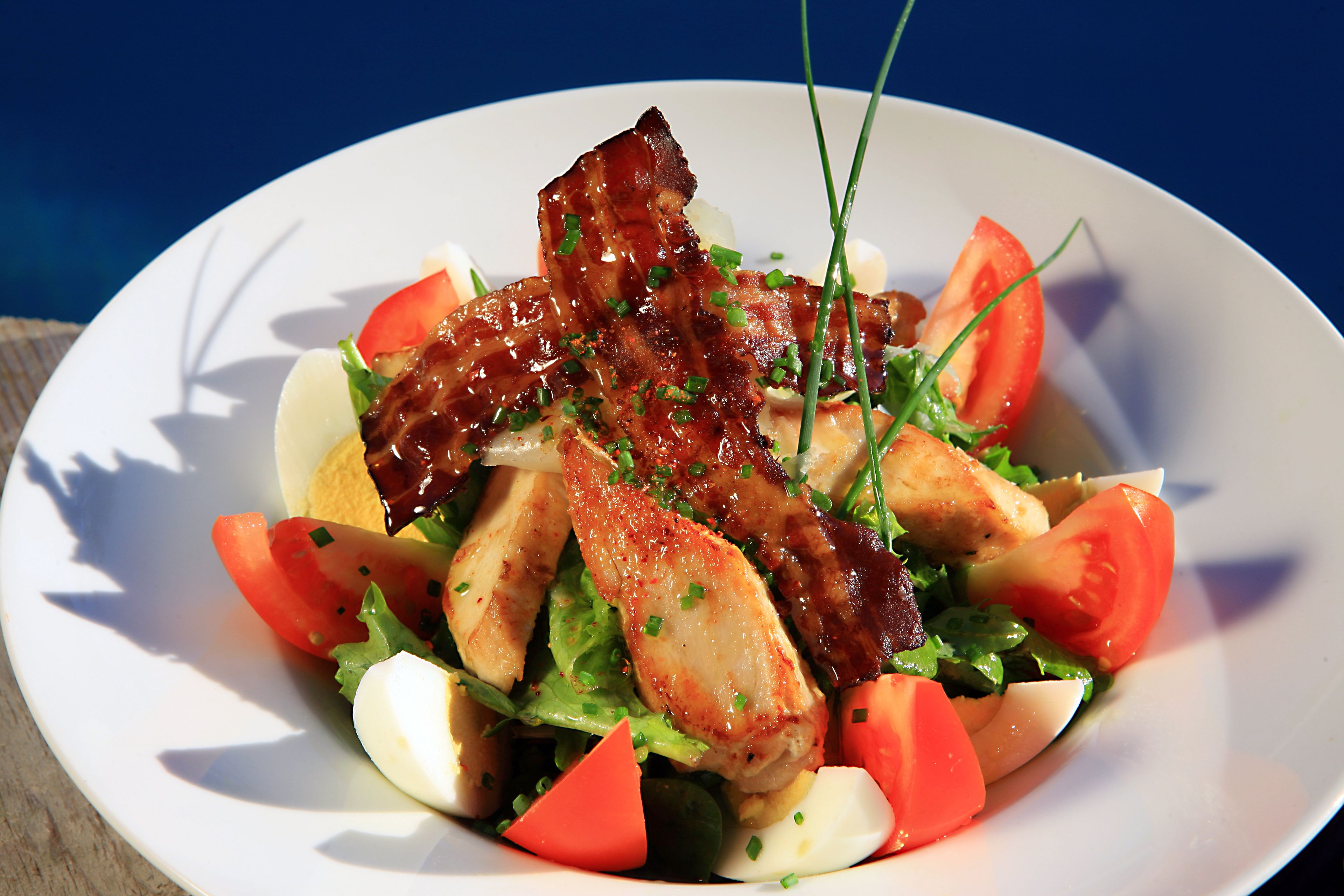 Ensalada amb bacon, tomàquets i verdures sobre un plat blanc.