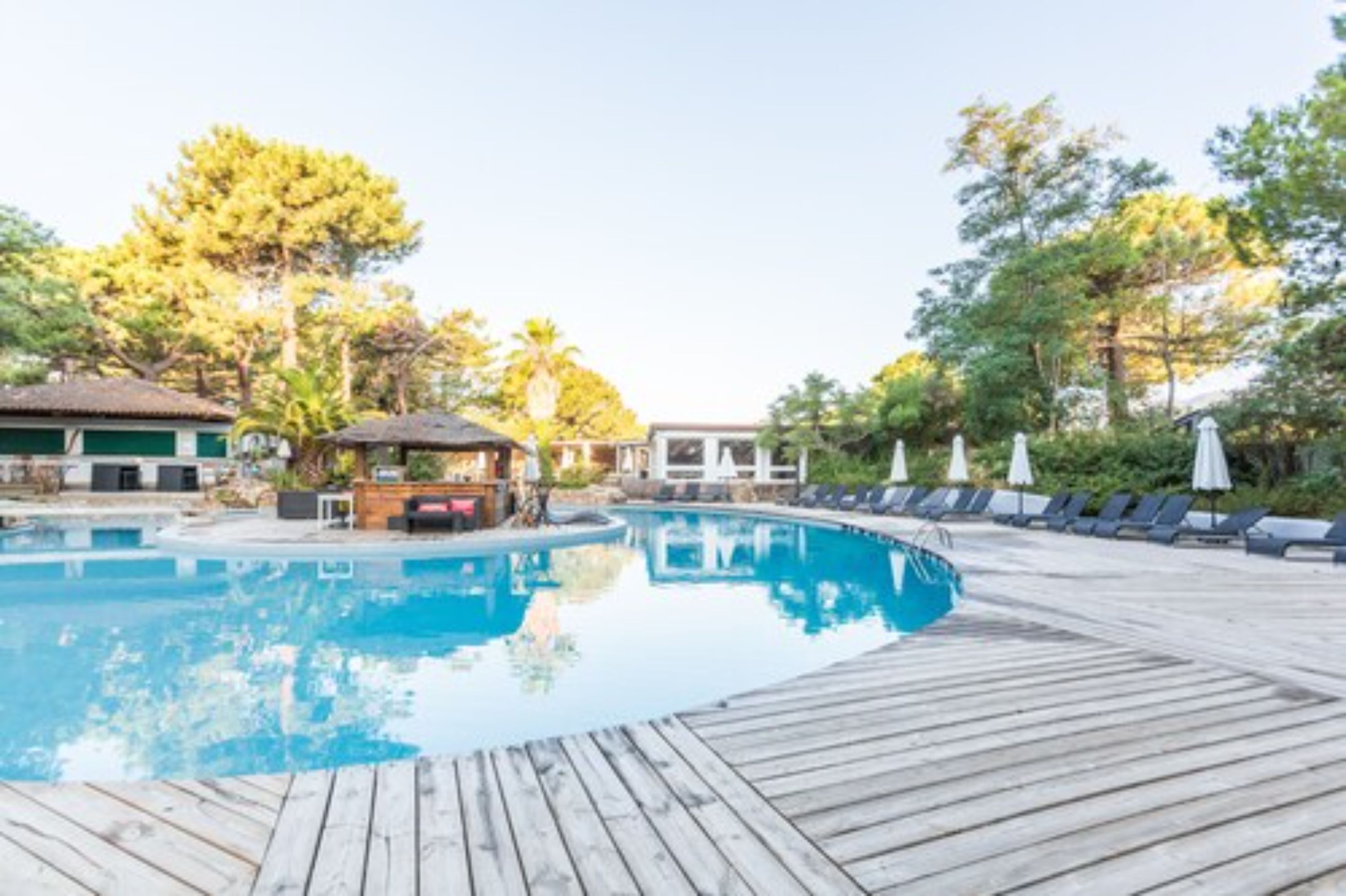 Una piscina con cubierta de madera, sillas de descanso y sombrillas.
