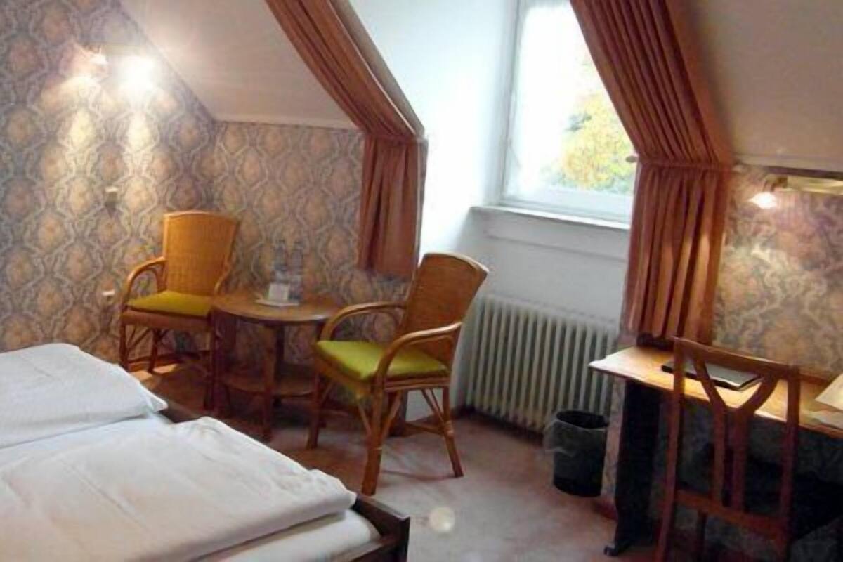 A room with a bed, two chairs, a small table, and a radiator.