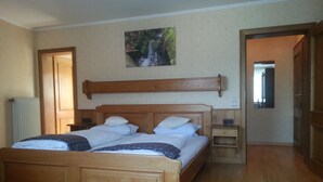 A bedroom with a wooden bed, a nightstand, a wall-mounted picture, and a radiator. - Hotel Ritschlay (Bollendorf)