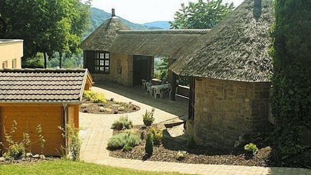 A rustic building with a thatched roof, a paved courtyard, and a small garden area. - Hotel Ritschlay (Bollendorf)