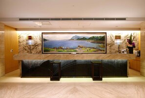 A reception area with a large TV screen displaying a scenic landscape, a marble counter, and a decorative vase with flowers.