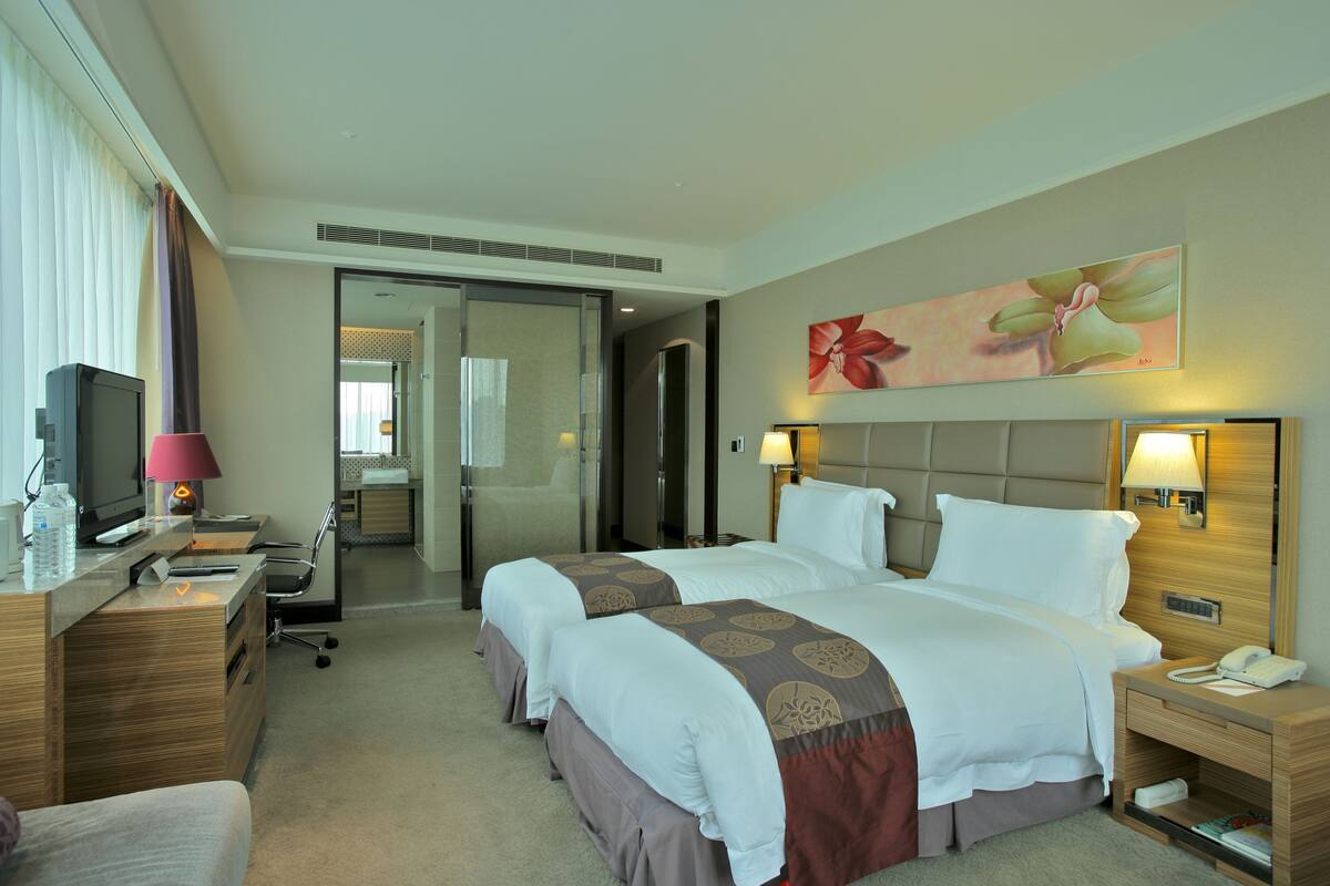 A hotel room with two beds, a desk with a computer, a TV, and a bathroom visible through an open door.