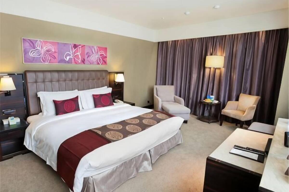 A hotel room with a large bed, two bedside tables with lamps, a chair, a desk, and a large window with curtains.