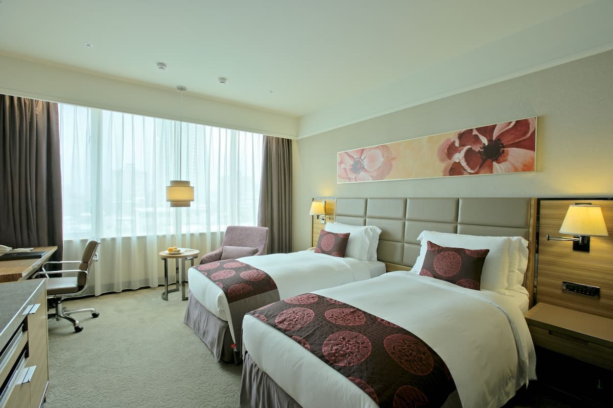 A hotel room with two beds, a desk, a chair, a small table, and a large window with curtains.