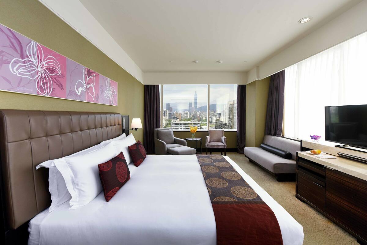 A hotel room with a large bed, a sofa, a TV, and a city view.