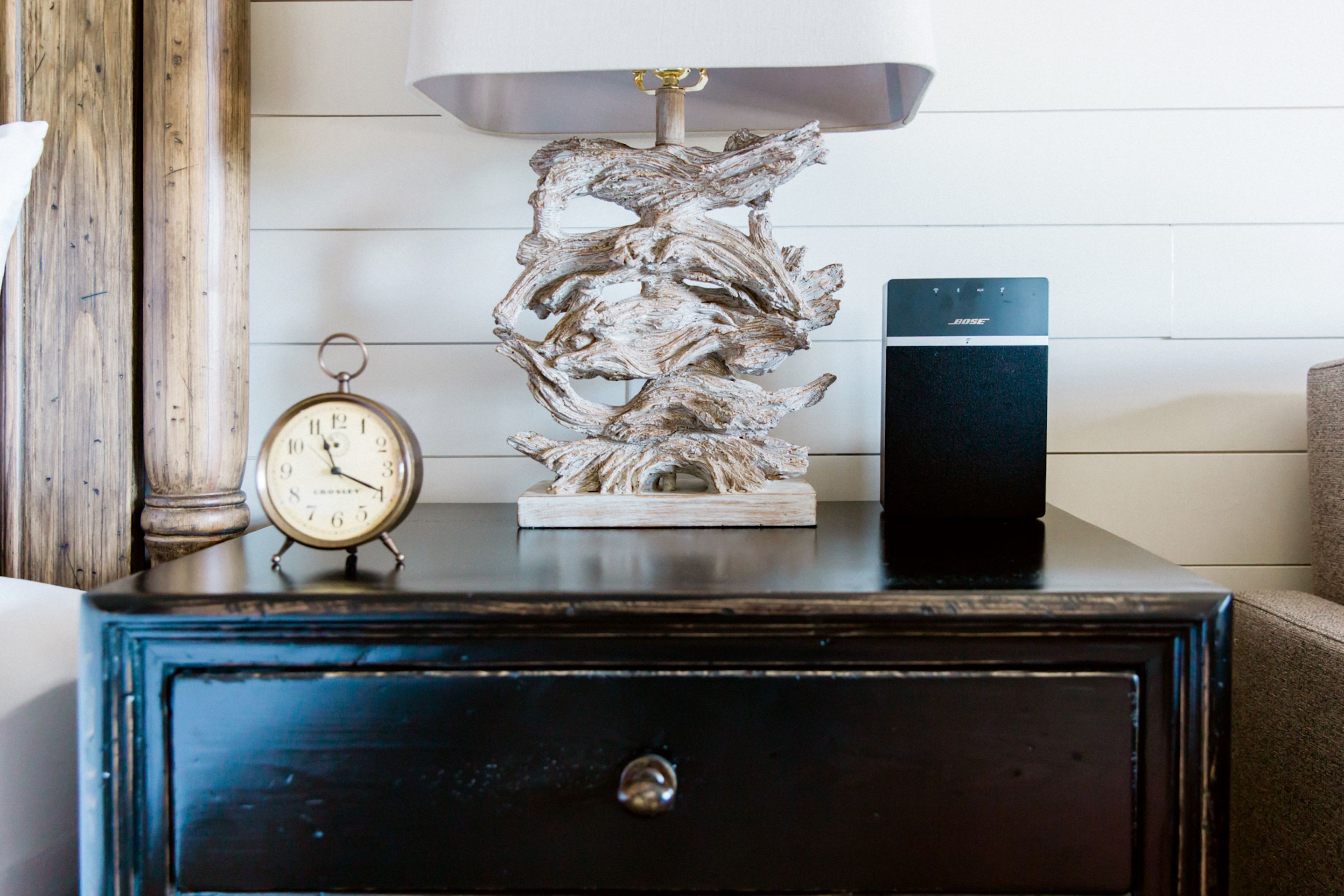 A wooden nightstand with a clock and a modern speaker.