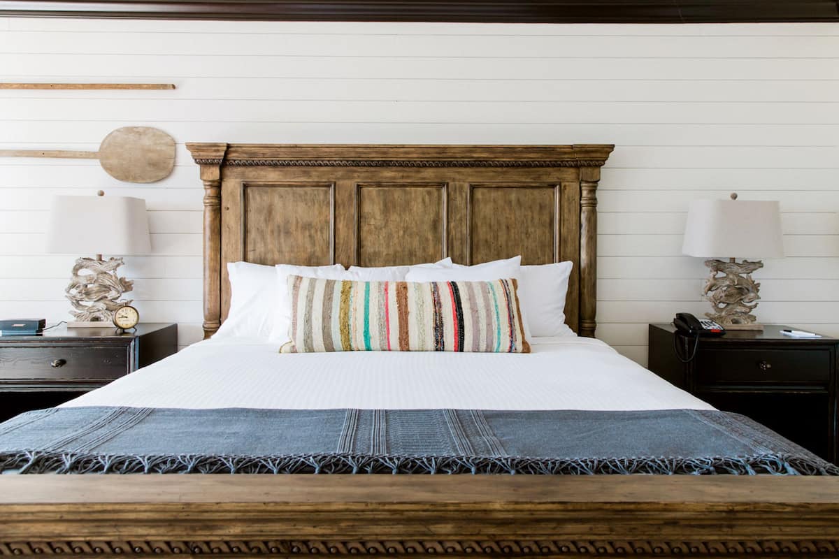 Ein ordentlich bezogenes Bett mit einem gestreiften Kopfkissen, einem Holz-Kopfteil und einer blauen Tagesdecke.