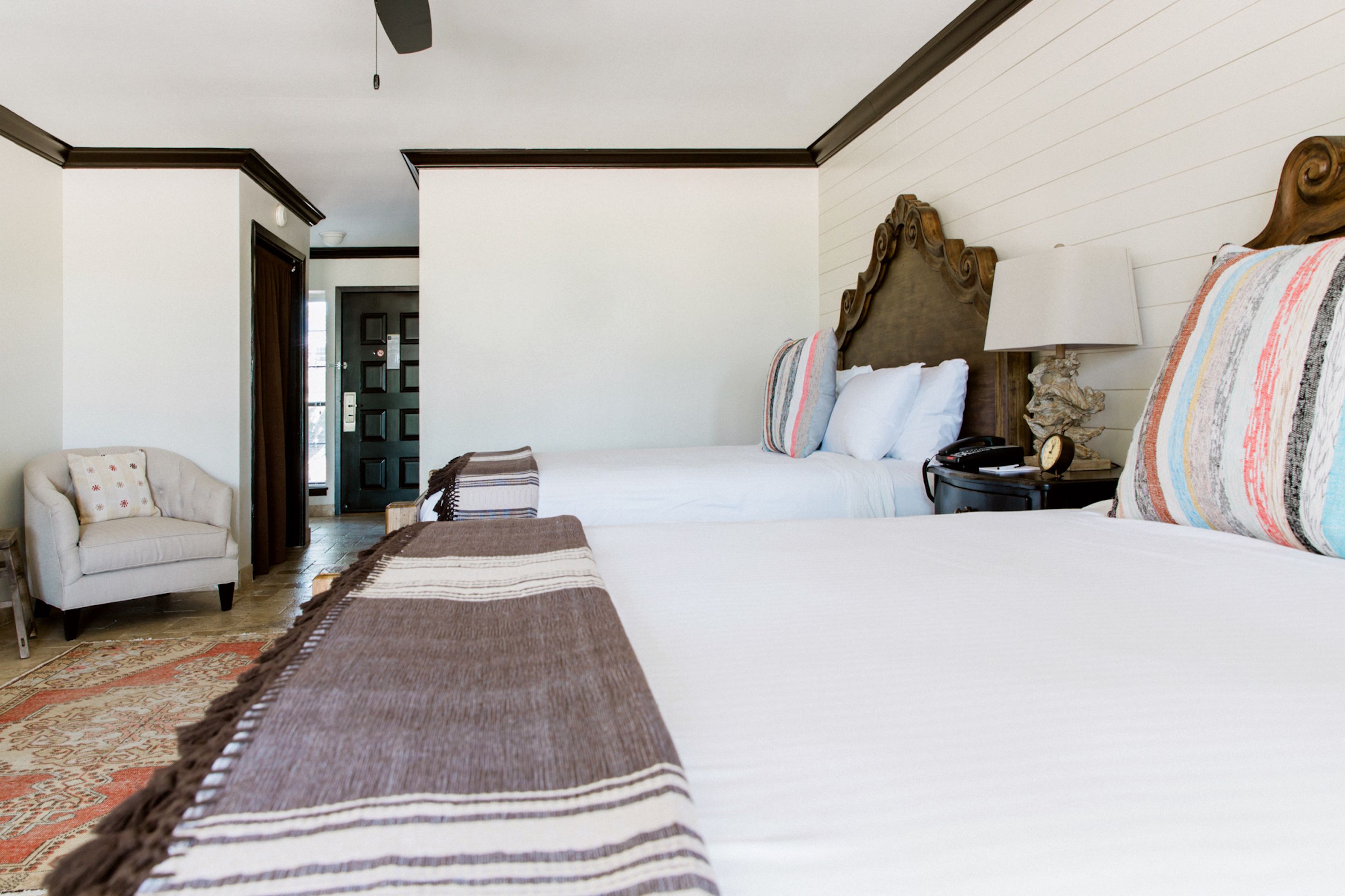 A hotel room with two beds, a sofa, a lamp, and a rug.