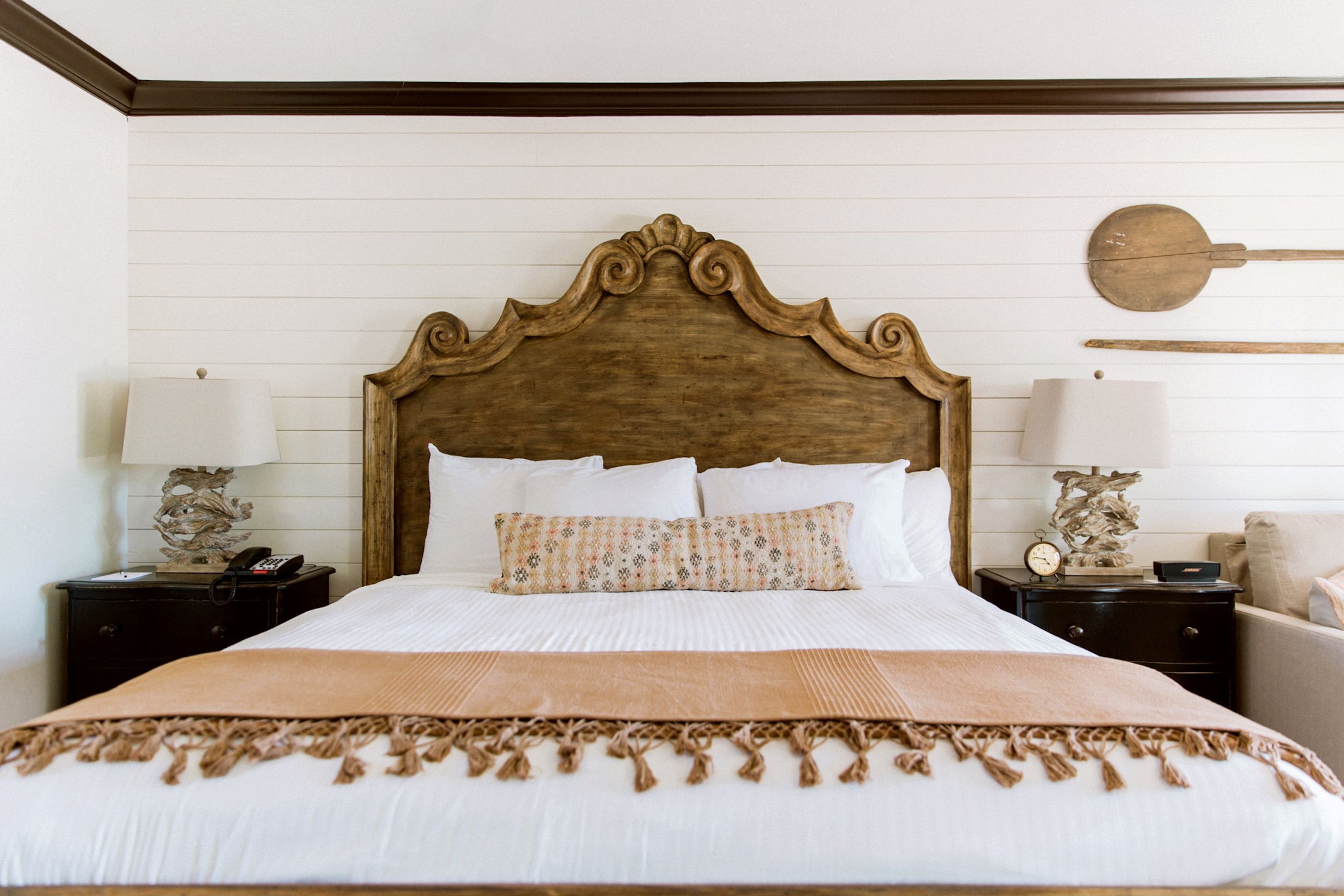 A neatly made bed with a wooden headboard, white bedding, and a brown throw blanket. There are two bedside tables with lamps and decorative items.