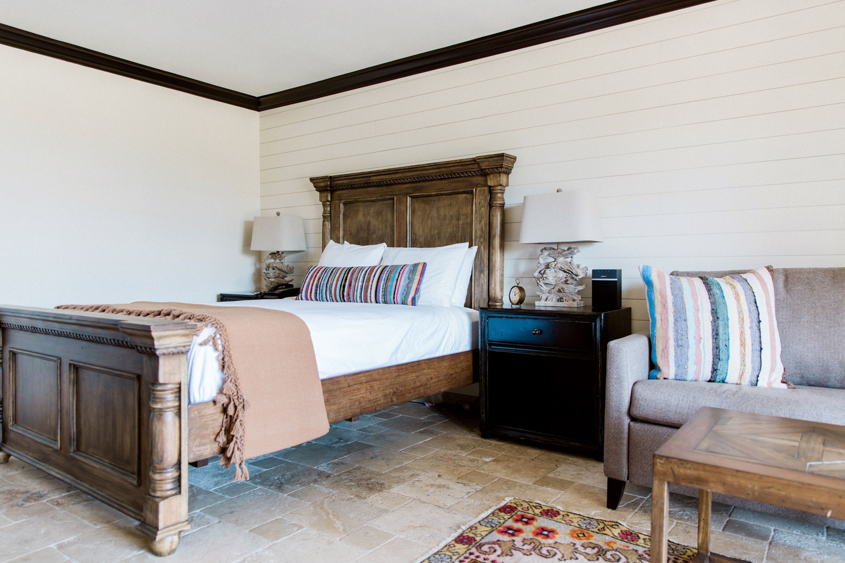 A bedroom with a wooden bed, a nightstand, a sofa, and a patterned rug.