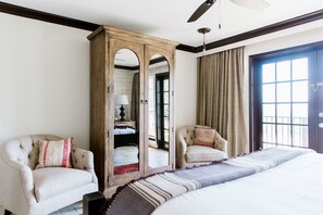 Une chambre d’hôtel avec un grand lit, deux fauteuils, une armoire en bois et une vue sur l’extérieur par une fenêtre.