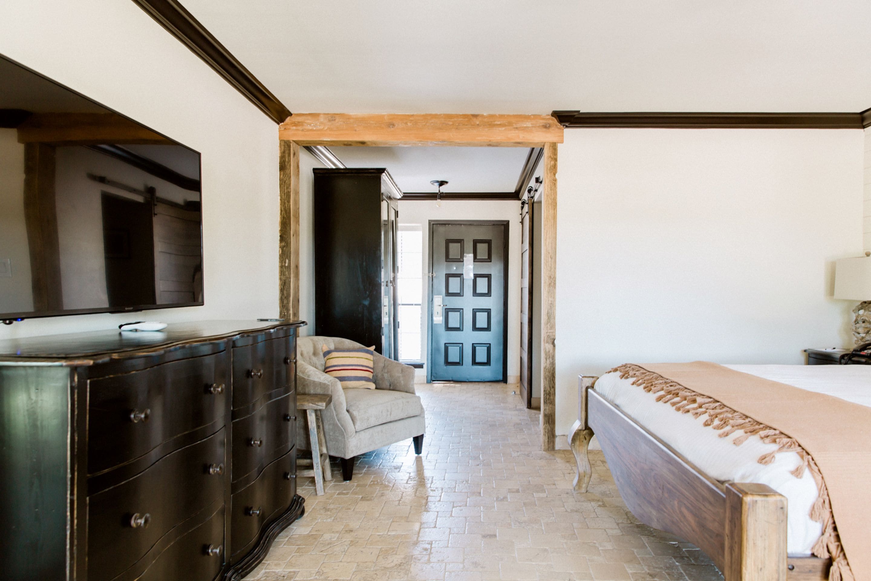 A bedroom with a bed, dresser, chair, and a door leading to another room.