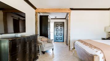 A bedroom with a bed, dresser, chair, and a door leading to another room.
