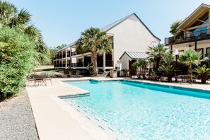 Un espace piscine avec une eau d’un bleu limpide, entouré de palmiers et bordé d’un bâtiment doté de balcons.