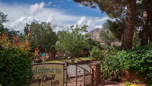 A wooden sign welcoming visitors to Baby Quilt Inn, featuring a rustic gate and surrounding greenery. - Baby Quail Inn (Sedona)