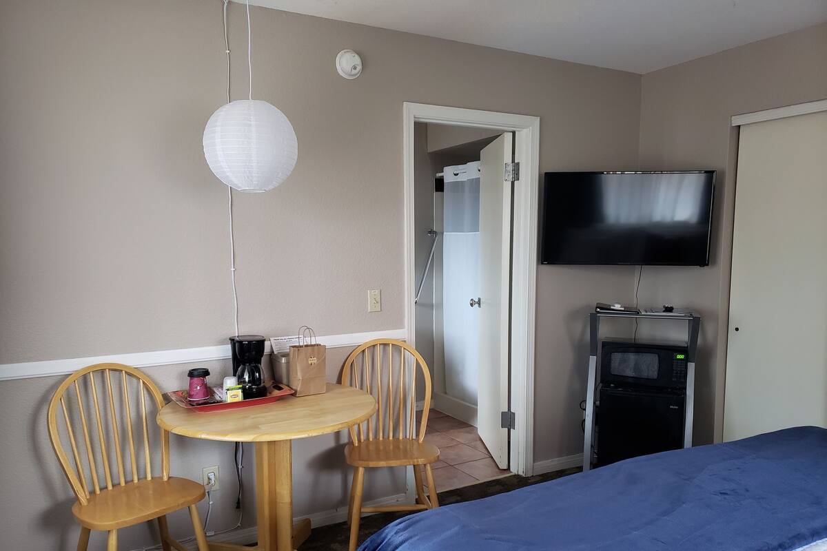 Quarto de hotel com cama, televisão, máquina de café e mesa com cadeiras.