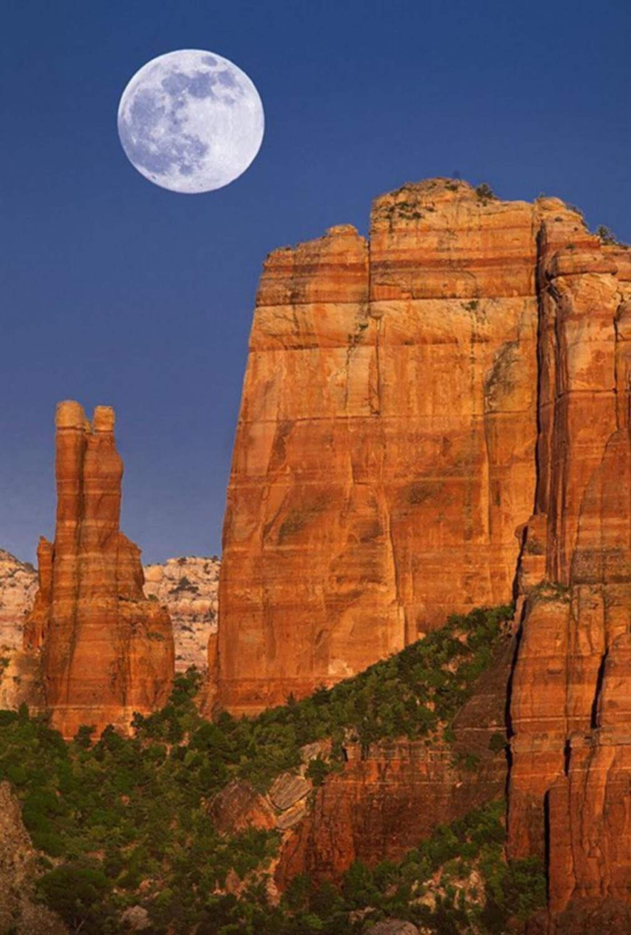 A large rock formation with a full moon in the sky.