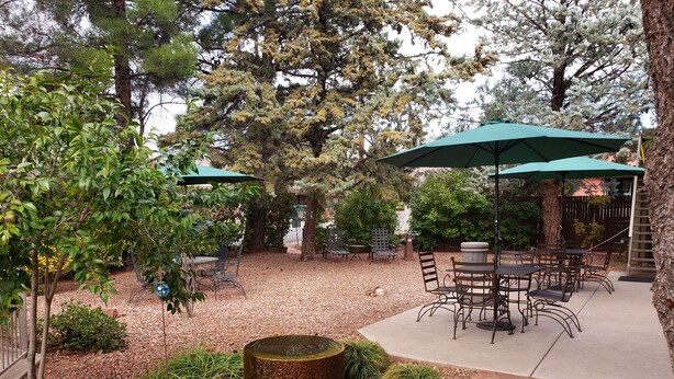 An outdoor patio area with tables and chairs under green umbrellas, surrounded by trees and a decorative fire pit. - Baby Quail Inn (Sedona)