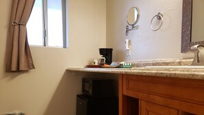 A bathroom with a vanity, a mirror, a sink, a trash bin, and a window with curtains. - Baby Quail Inn (Sedona)