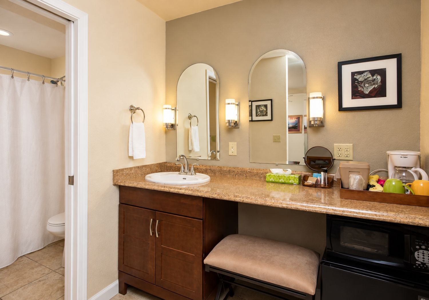 A bathroom with a sink, mirrors, a toilet, a cabinet, and a coffee maker.