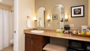 A bathroom with a sink, mirrors, a toilet, a cabinet, and a coffee maker.