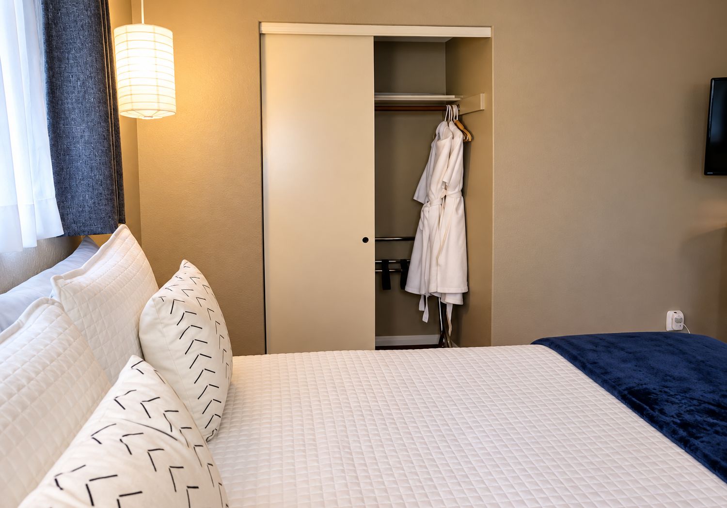 Une chambre d’hôtel avec un lit, un peignoir suspendu à un porte-manteau et une table de chevet.