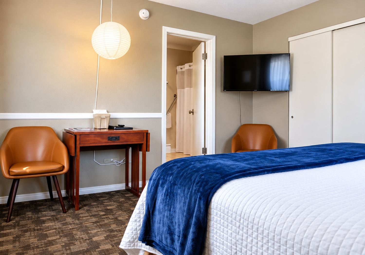 Una camera d'albergo con un letto, due poltrone, una scrivania, una televisione e un bagno.