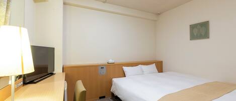 Habitación de hotel con cama, escritorio con lámpara, televisor y panel de control en la pared.
