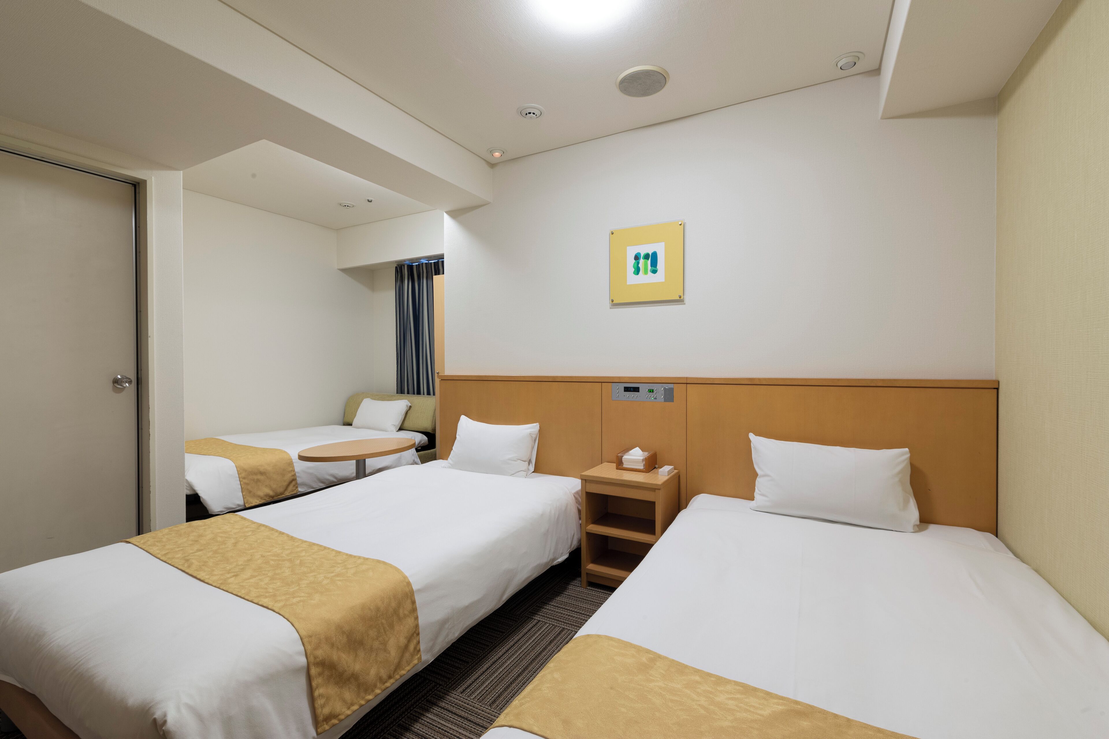 Habitación de hotel con dos camas, una mesita, una mesita de noche y un reloj en la pared.