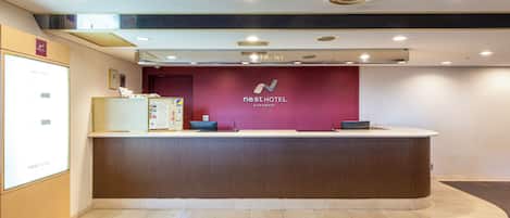 Una recepción de hotel con diseño moderno, un panel informativo digital y un letrero que indica la zona de recepción.