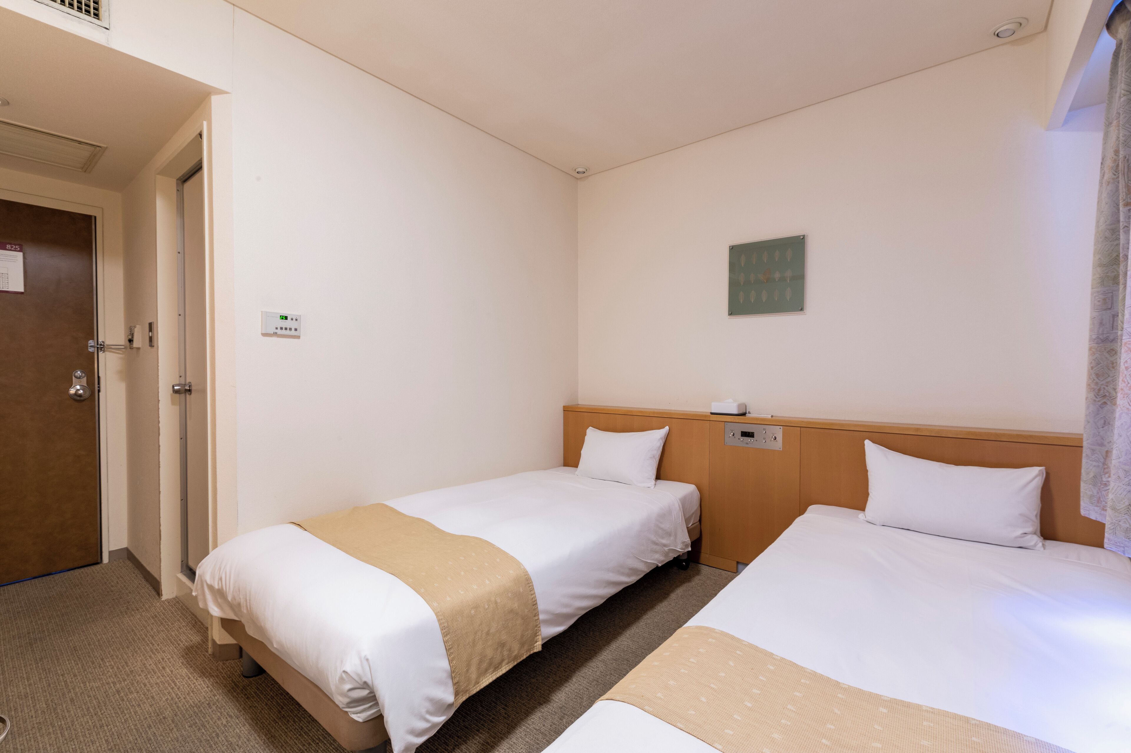 Habitación de hotel con dos camas individuales, cabecera de madera, un pequeño reloj de pared y una puerta con cerradura.