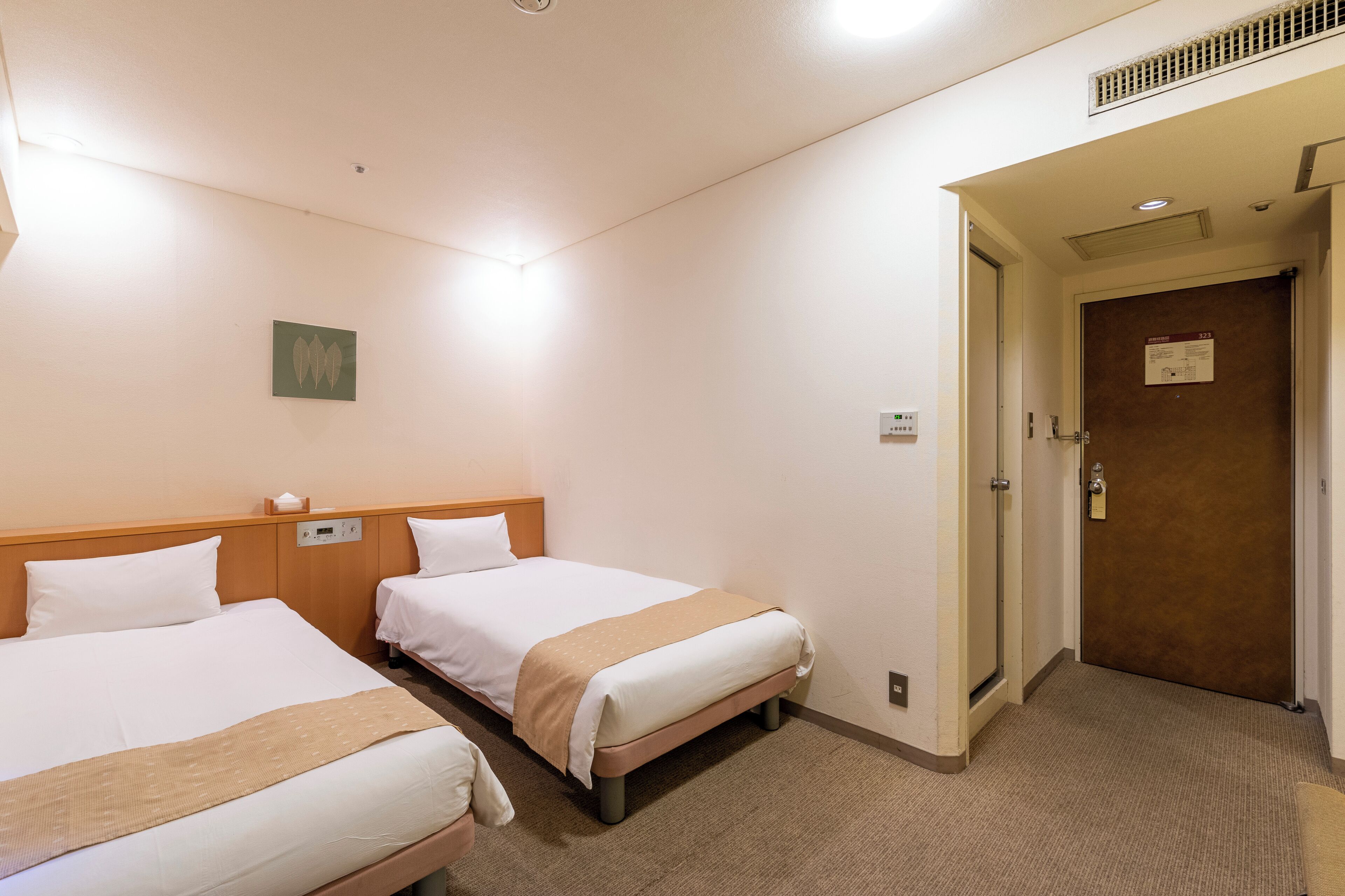 A hotel room with two beds, a wooden headboard, a beige carpet, and a door with a sign.