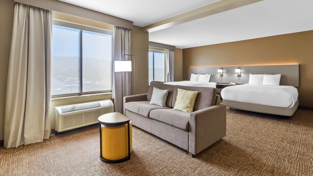 A hotel room with a large bed, a sofa, a small table, and a view of the city. - Comfort Suites El Paso West (El Paso)