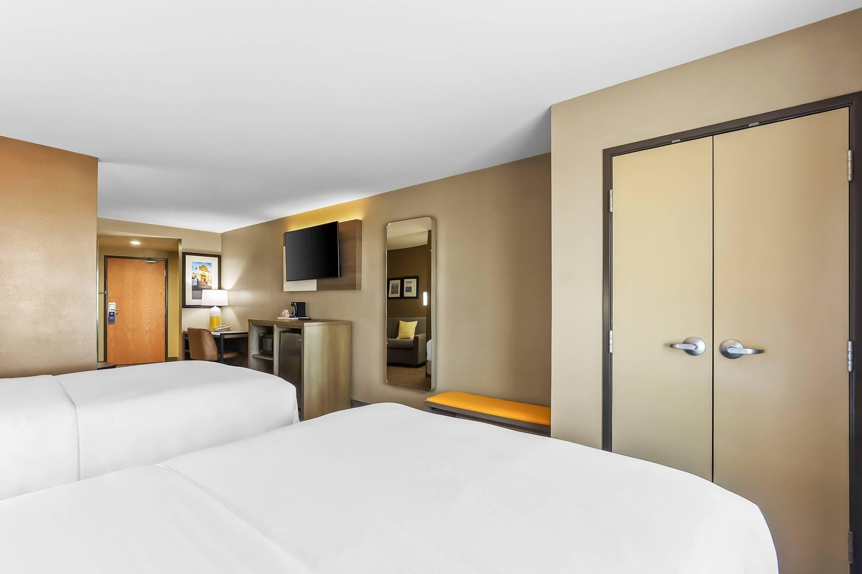 Une chambre d’hôtel avec deux lits, un bureau, une chaise, une télévision, une armoire et un miroir.