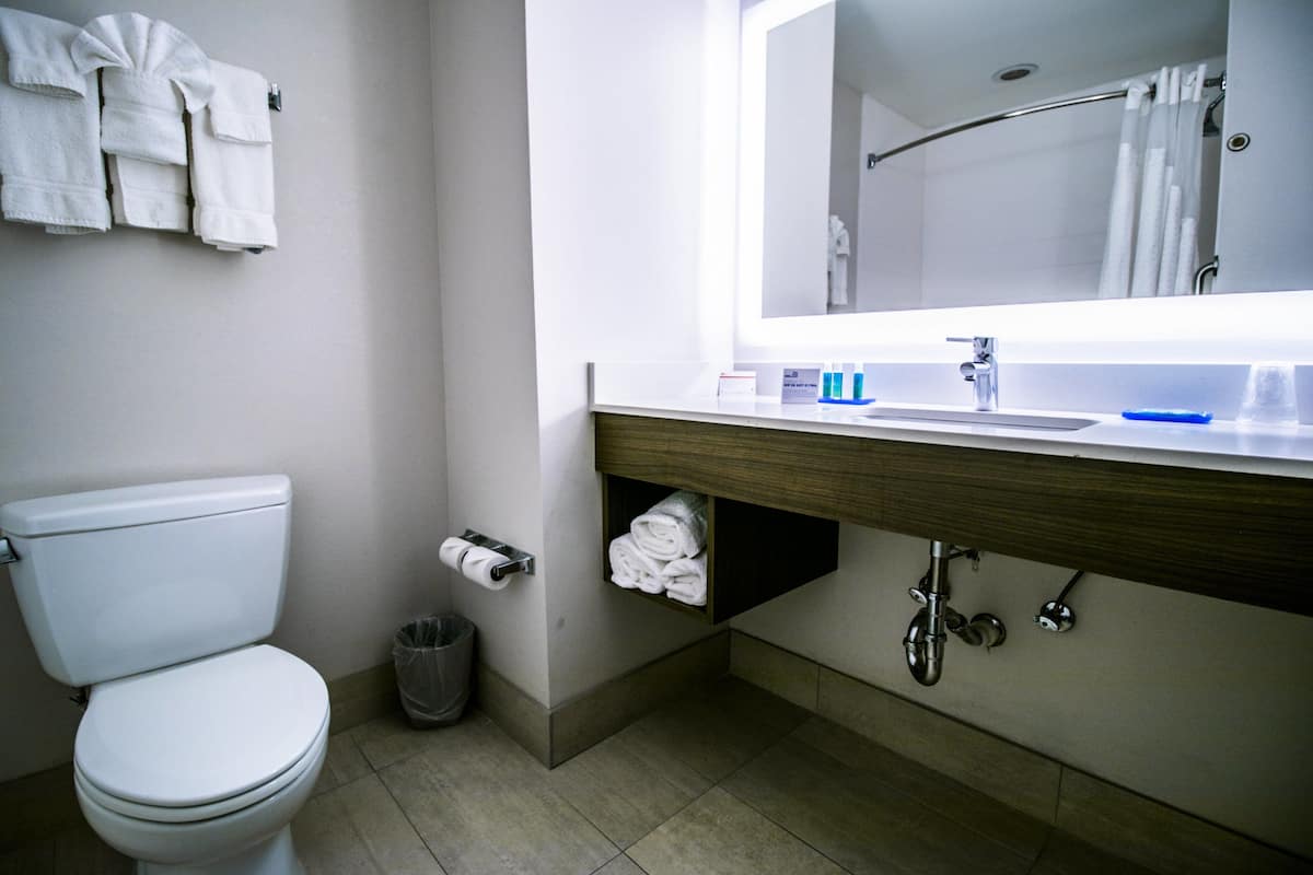 Une salle de bain moderne équipée de toilettes, d’un lavabo avec un miroir et d’un porte-serviettes.