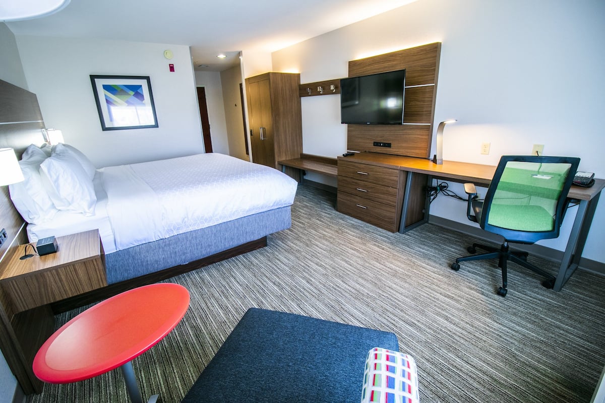 Une chambre d’hôtel avec un lit, un bureau, une chaise, une télévision et une petite table avec une lampe.