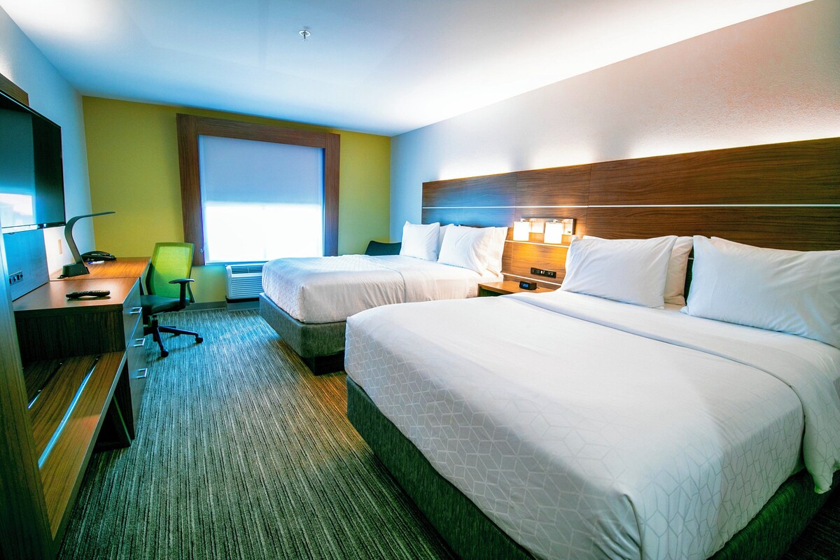 A hotel room with two beds, a desk with a chair, a TV, and a window.
