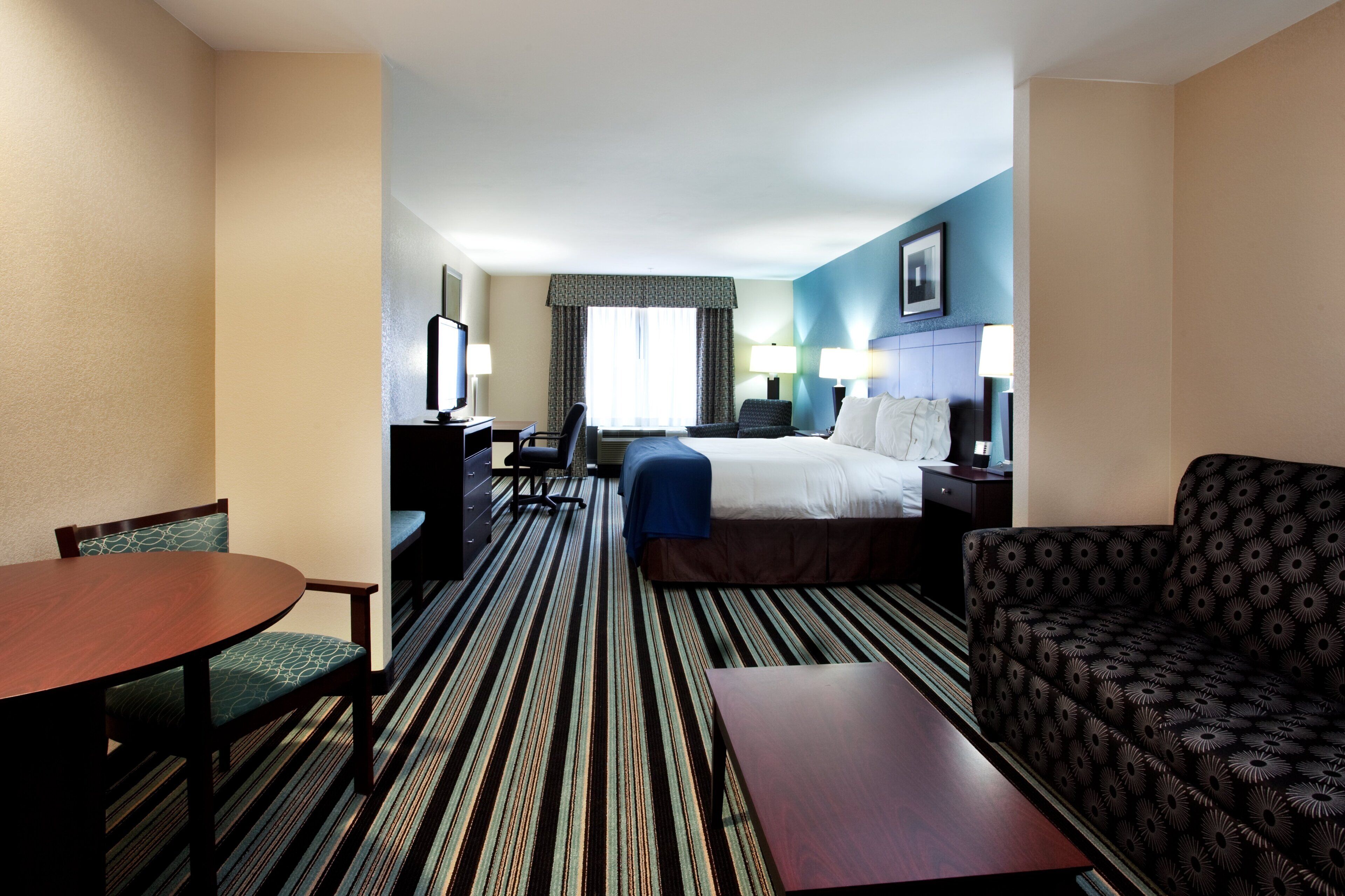 A hotel room with a bed, a desk, a chair, a table, and a sofa.