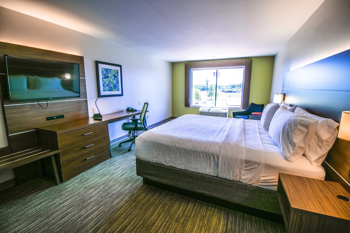 Une chambre d’hôtel avec un lit, un bureau, une chaise, une télévision et une fenêtre.