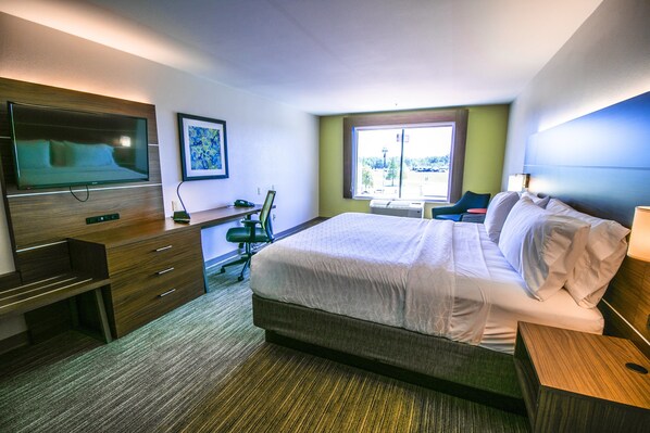 A hotel room with a bed, a desk, a chair, a TV, and a window.